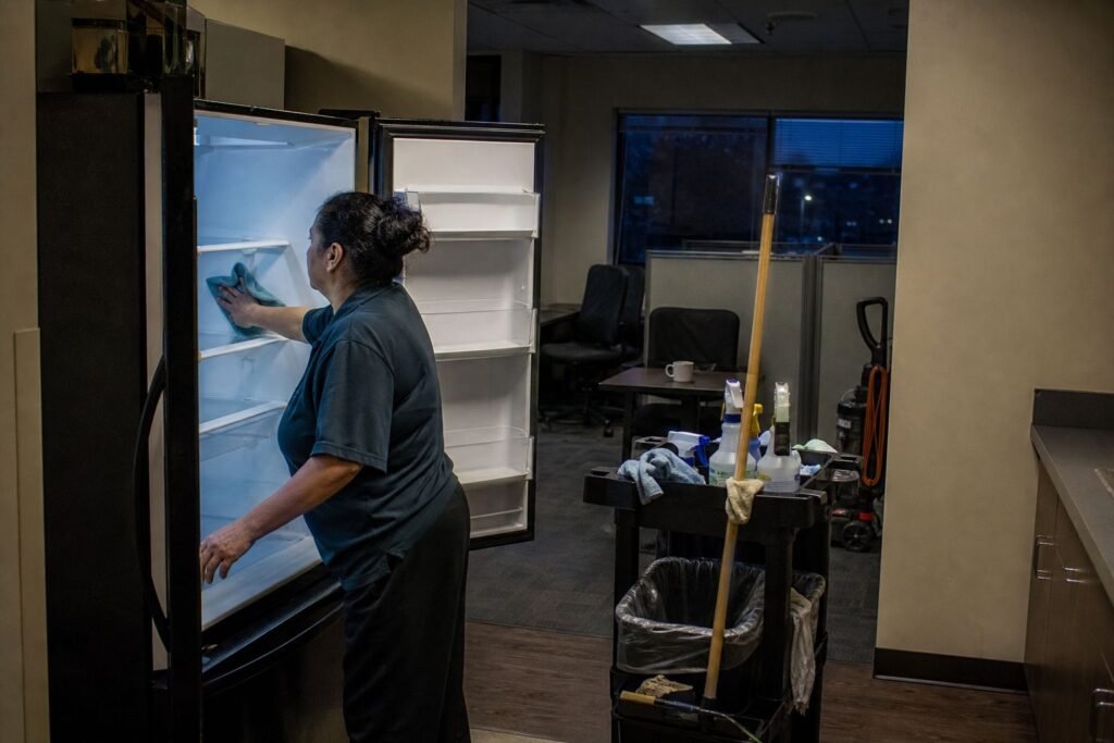 Cleaner wiping the inside of an office refrigerator